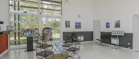 A spacious room with a large window, a reception desk, several chairs, a small table, and informational posters on the walls.