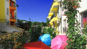 A courtyard with colorful umbrellas, a yellow building with balconies, and a clear blue sky. - Luxury 2-Bedroom Apartment in MiniSmart Complex RainbowGarden (Balchik)