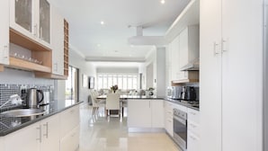 A modern kitchen with white cabinets, a black countertop, and a dining area with a table and chairs. - Villa Balmoral 14 (Cape Town)