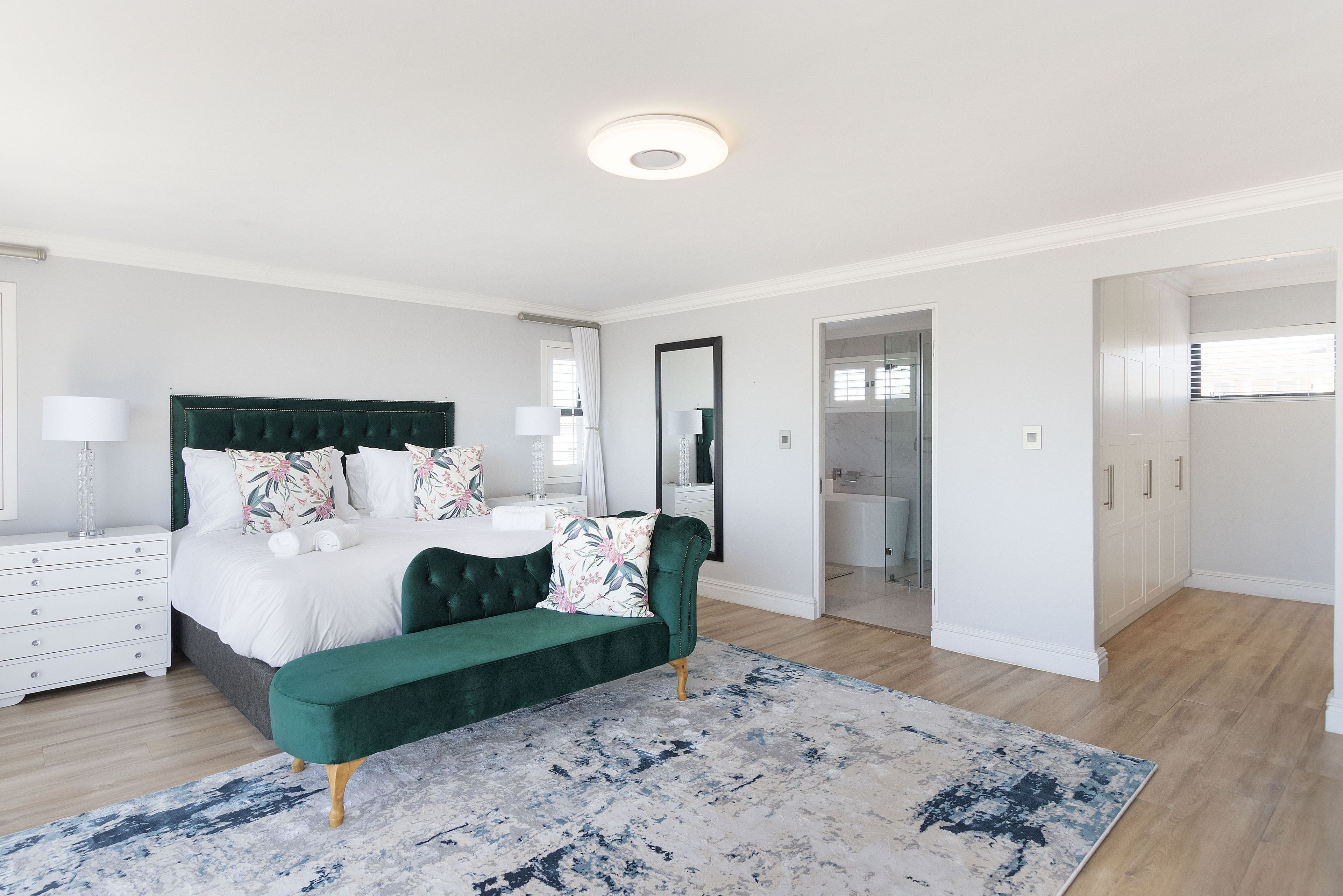 Un dormitorio moderno con una cama grande, un banco tapizado en verde y una alfombra estampada.