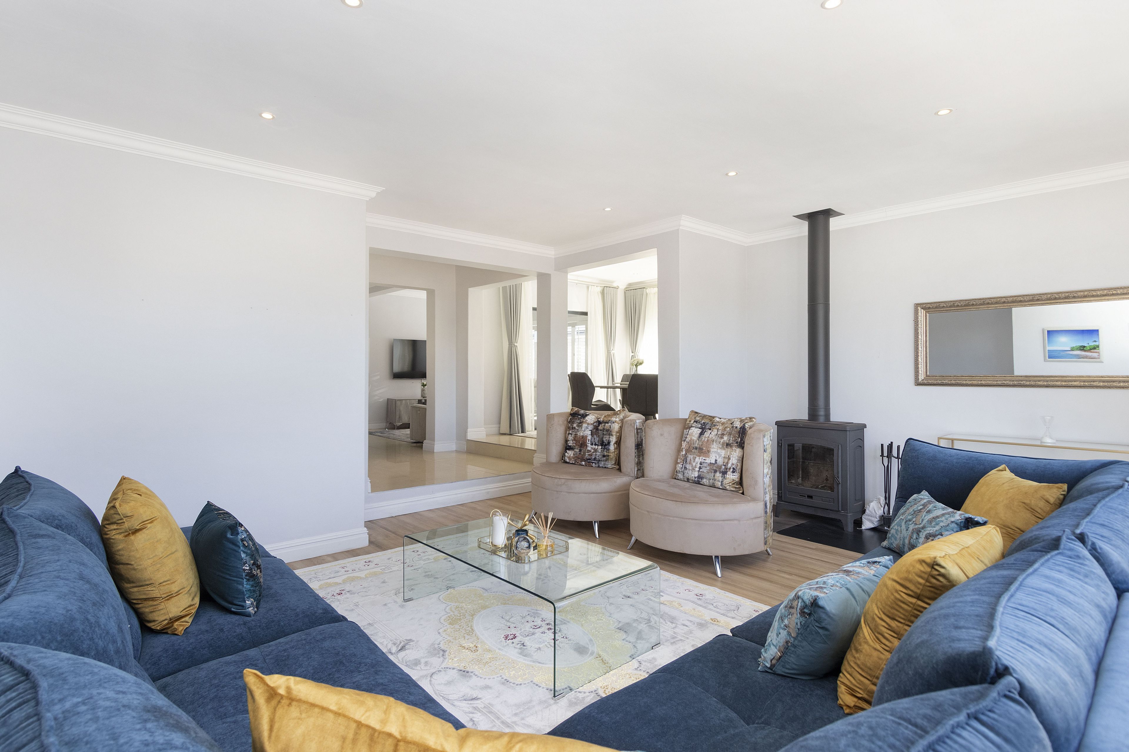 A modern living room with a blue sofa, a glass coffee table, and a fireplace.