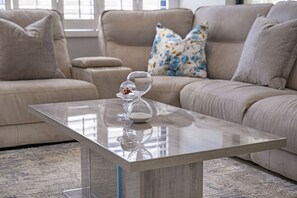 A modern living room with a glass-top coffee table, beige sofa, and floral pillows.