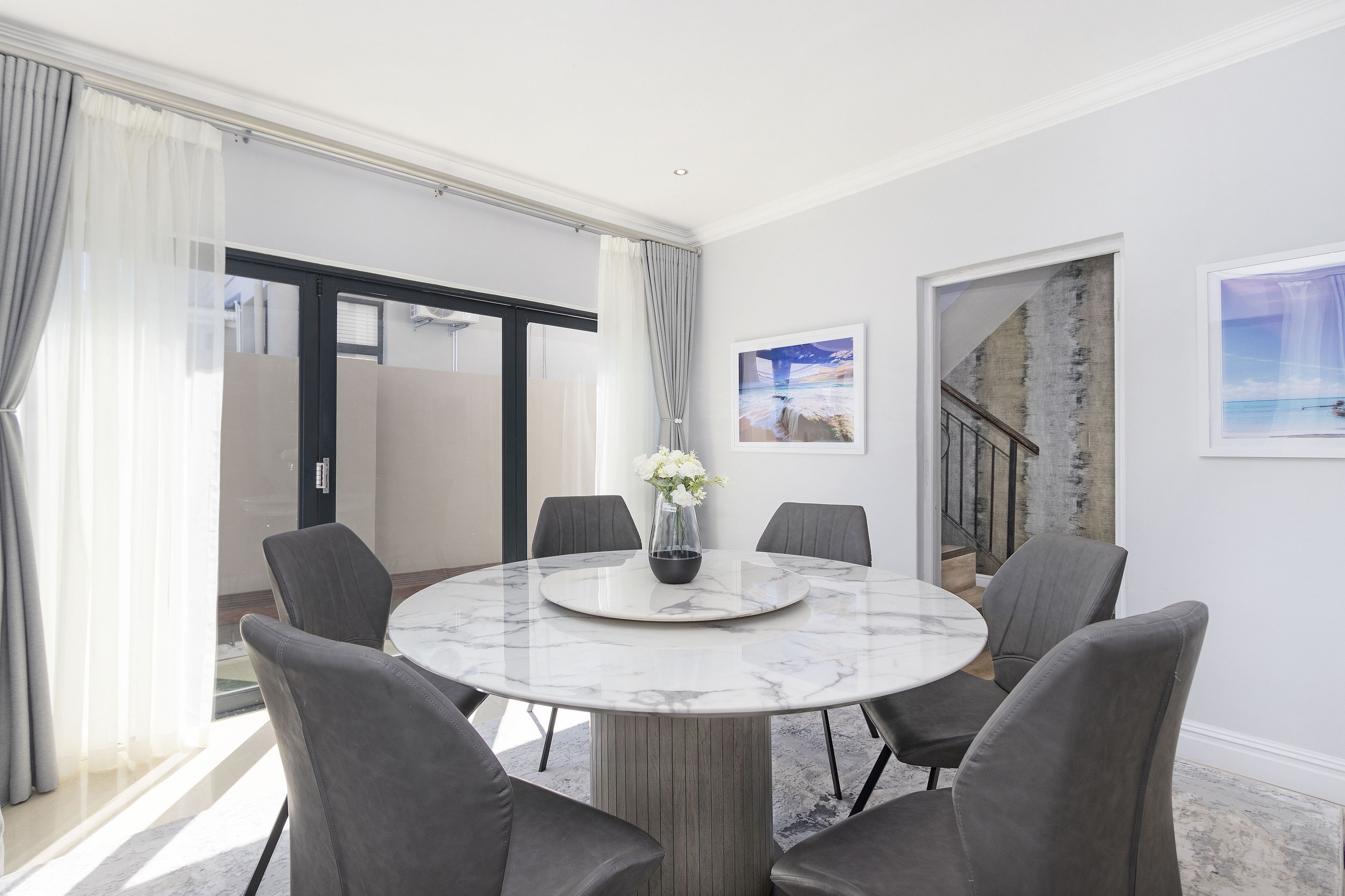 A modern dining area with a marble table, grey upholstered chairs, and a vase with white flowers.