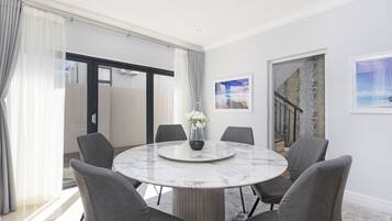 A modern dining area with a marble table, grey upholstered chairs, and a vase with white flowers.