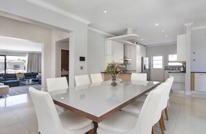 Un salón espacioso con una gran mesa de comedor, sillas blancas y un conjunto de sofás.