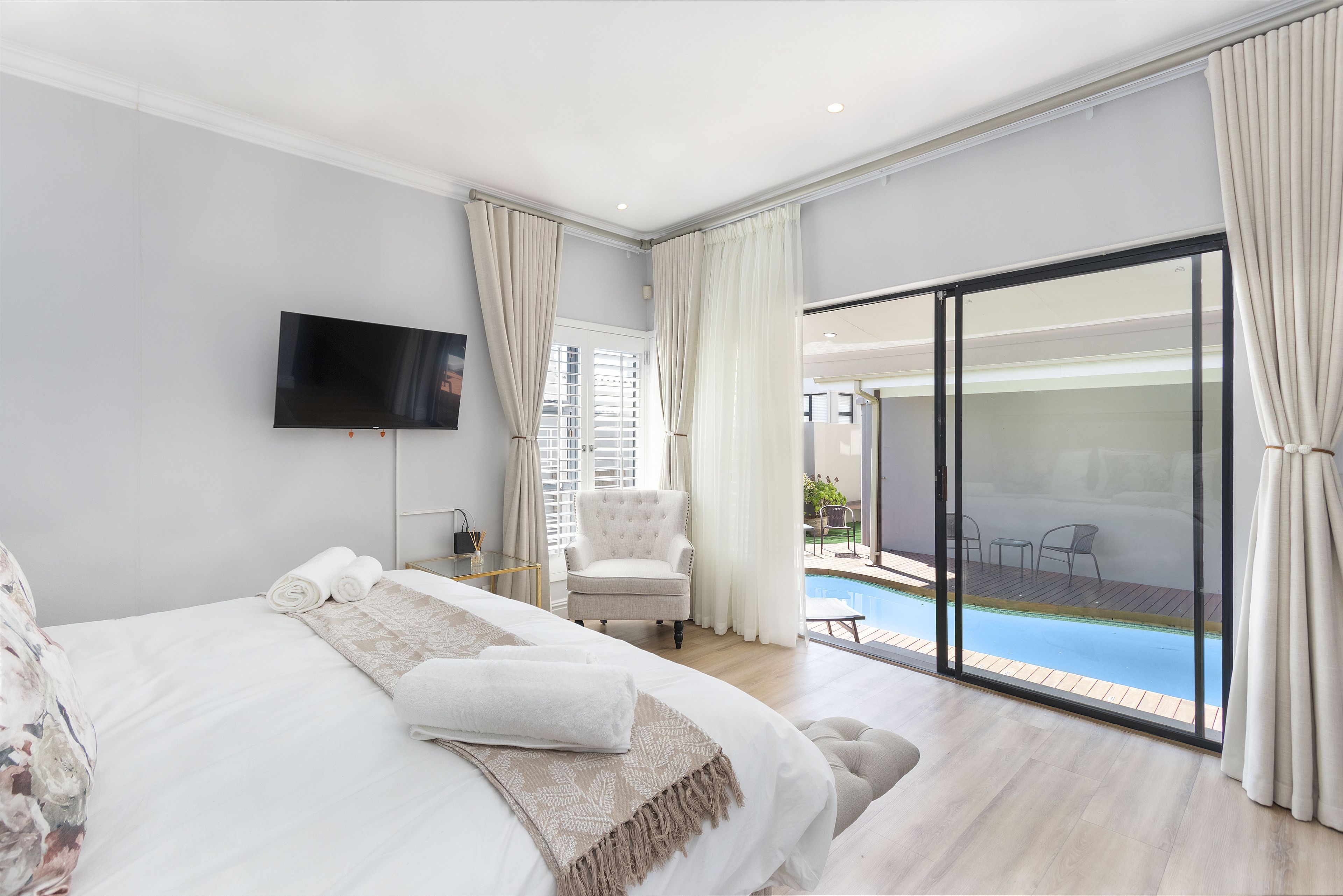 A bedroom with a large bed, a flat-screen TV, a chair, and a sliding glass door leading to a pool area.