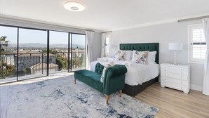 A spacious bedroom with a large window, a green upholstered bench, a white bed with decorative pillows, and a white nightstand. - Villa Balmoral 14 (Cape Town)