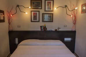 A bedroom with a dark headboard, a bed with white bedding, wall-mounted lights, and framed artwork.
