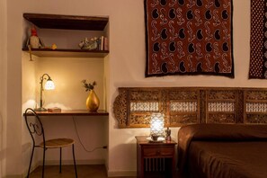 Une pièce comprenant un bureau, une chaise, une table de chevet, une lampe, un élément décoratif mural et un lit.