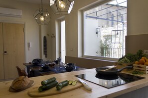 A modern kitchen with a large window, a wooden cutting board with vegetables, a frying pan, and a built-in stove.
