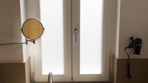 Un baño con espejo, ventana y secador de pelo en la pared.