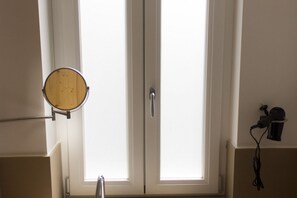 A bathroom with a mirror, a window, and a hairdryer on the wall.