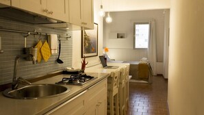 A modern kitchen with a stainless steel sink, white cabinets, and a tiled backsplash. There is a window with curtains and a laptop on the counter. - Sui Tetti di Napoli - panoramic terrace 3 (Napoli)