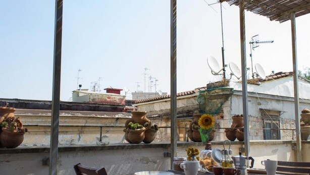 A rooftop terrace with terracotta pots, a table with a plate, cups, and a coffee pot. - Sui Tetti di Napoli - panoramic terrace 3 (Napoli)