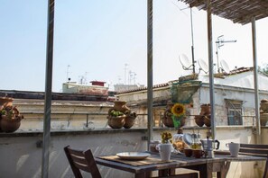 Une terrasse sur le toit, ornée de pots en terre cuite, avec une table sur laquelle se trouvent une assiette, des tasses et une cafetière.