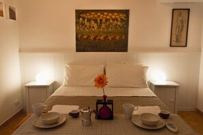 Une chambre d’hôtel avec un lit, des tables de chevet, un vase avec une fleur et un tableau au mur.