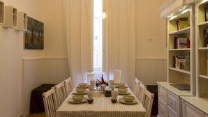 A dining area with a table set for four, chairs, a bookshelf, and a painting on the wall. - Sui Tetti di Napoli - in the heart of authentic naples (Napoli)