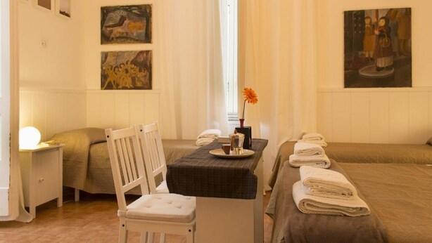 A hotel room with a bed, a chair, a table with a vase, and artwork on the walls. - Sui Tetti di Napoli - in the heart of authentic naples (Napoli)