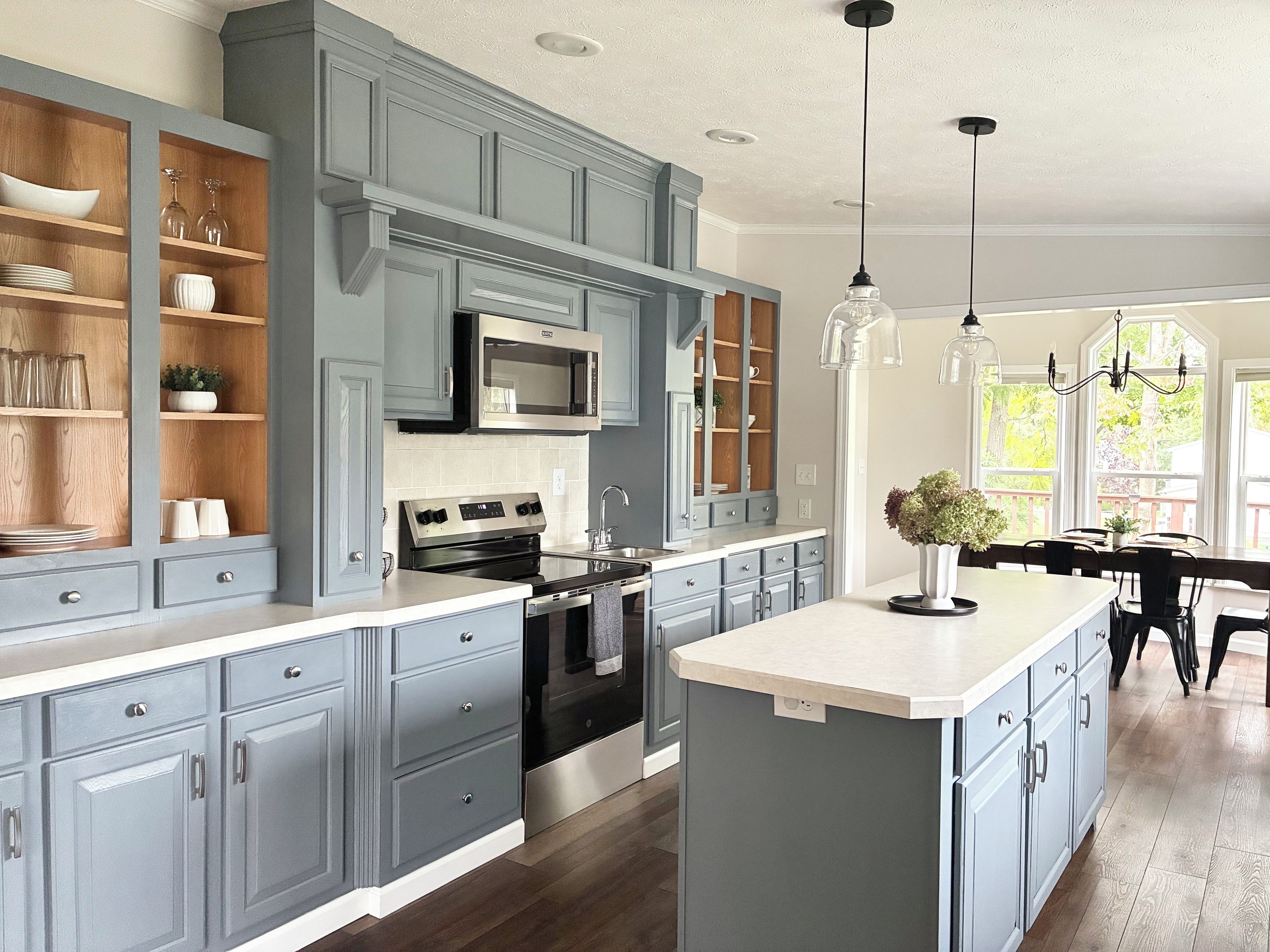 A kitchen with grey cabinetry, a central island, stainless steel appliances, and pendant lighting.