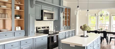 A kitchen with grey cabinetry, a central island, stainless steel appliances, and pendant lighting.
