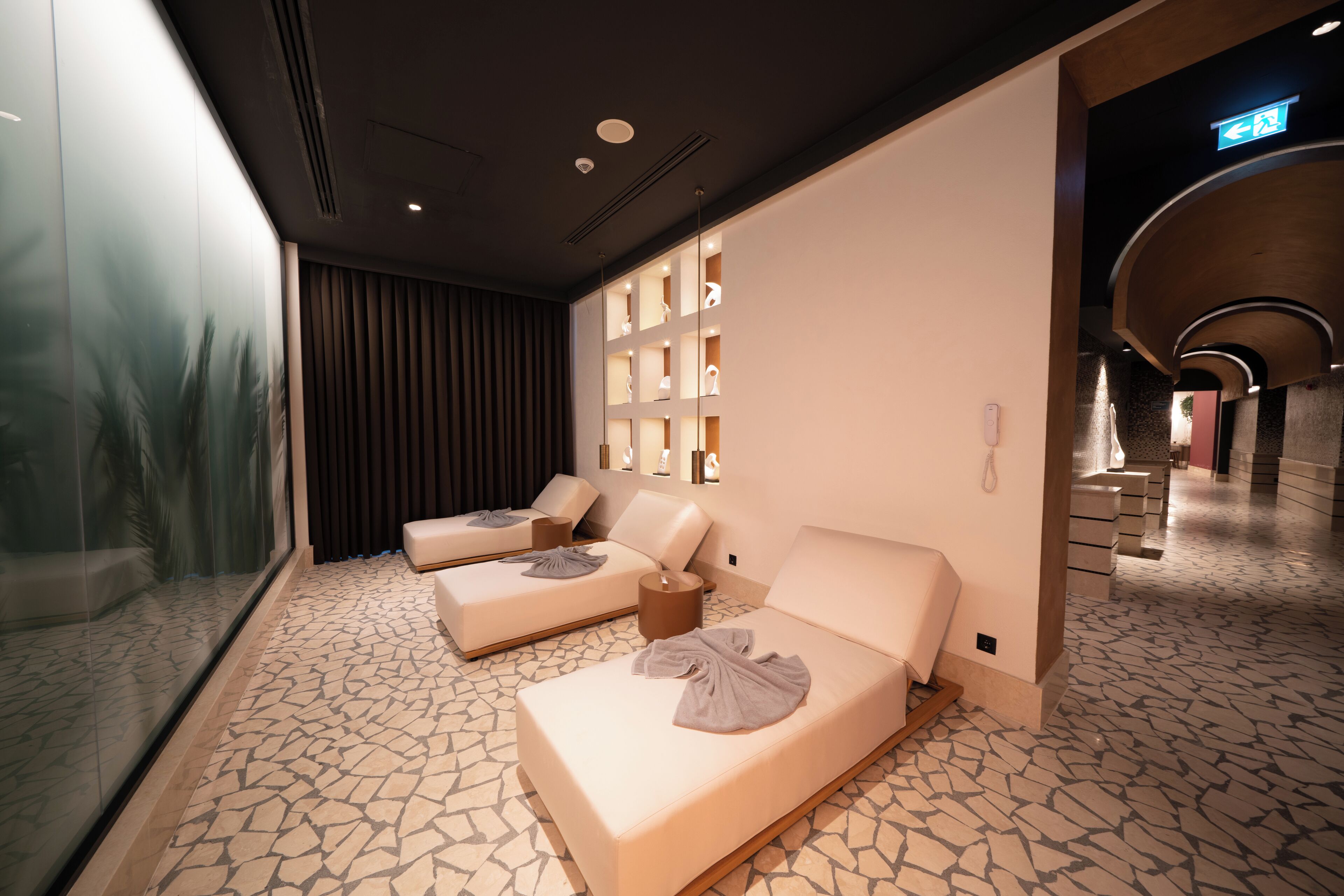 A spa room with two massage beds, a glass wall, and a tiled floor.