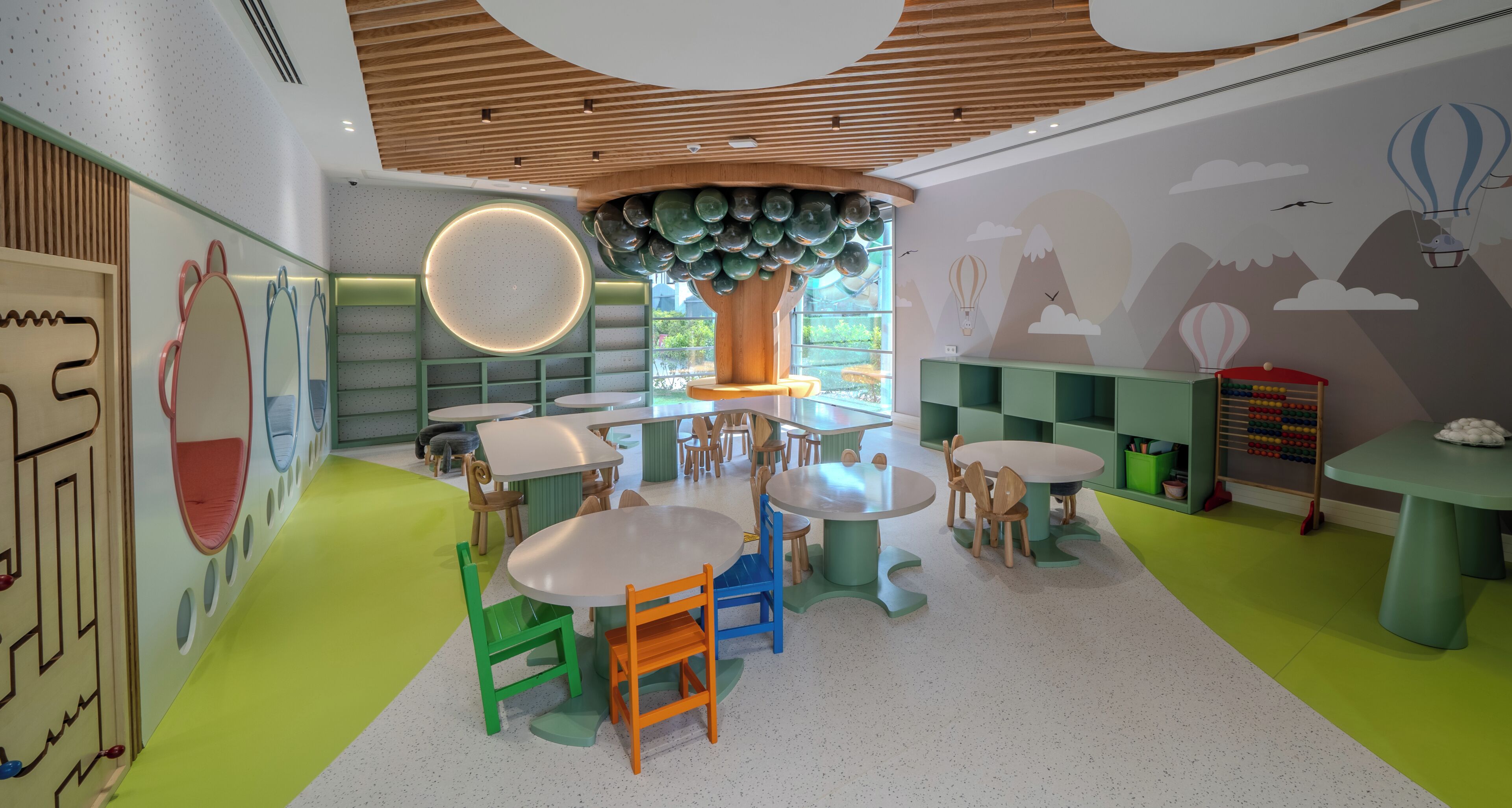 A children's play area with round tables, chairs, and a large tree-like structure.