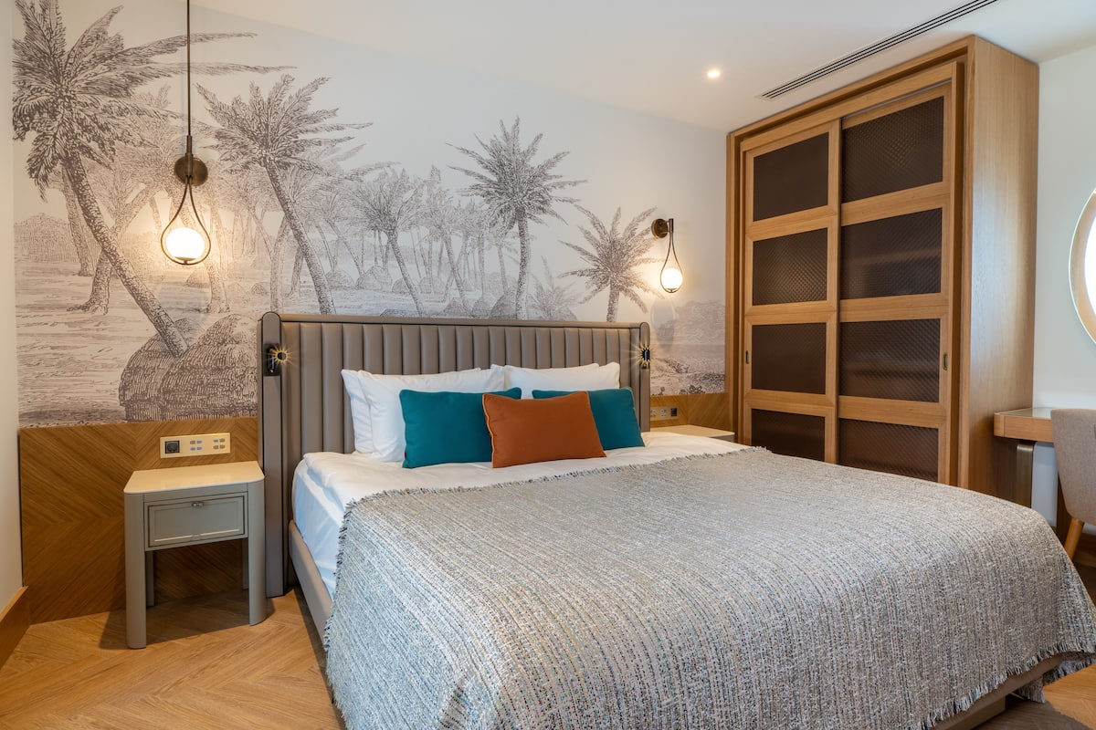 Une chambre à coucher comprenant un lit, des tables de chevet, une fresque murale et une armoire.