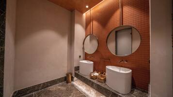 Un baño con dos lavamanos, un espejo y un cubo de basura.