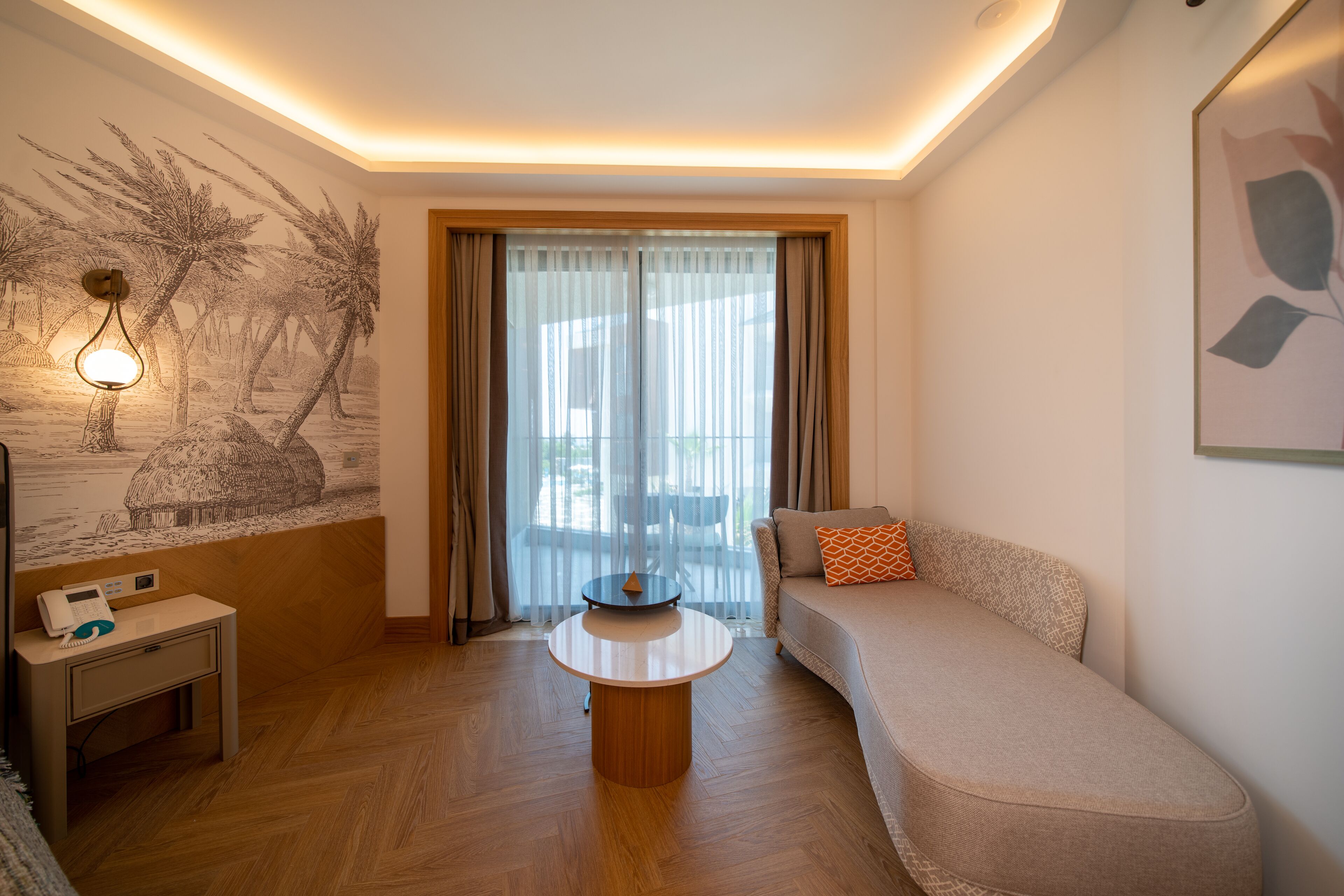 Uma sala de estar moderna com uma mesa de centro redonda, um sofá com almofada laranja, uma luminária de parede e uma janela grande com cortinas translúcidas.