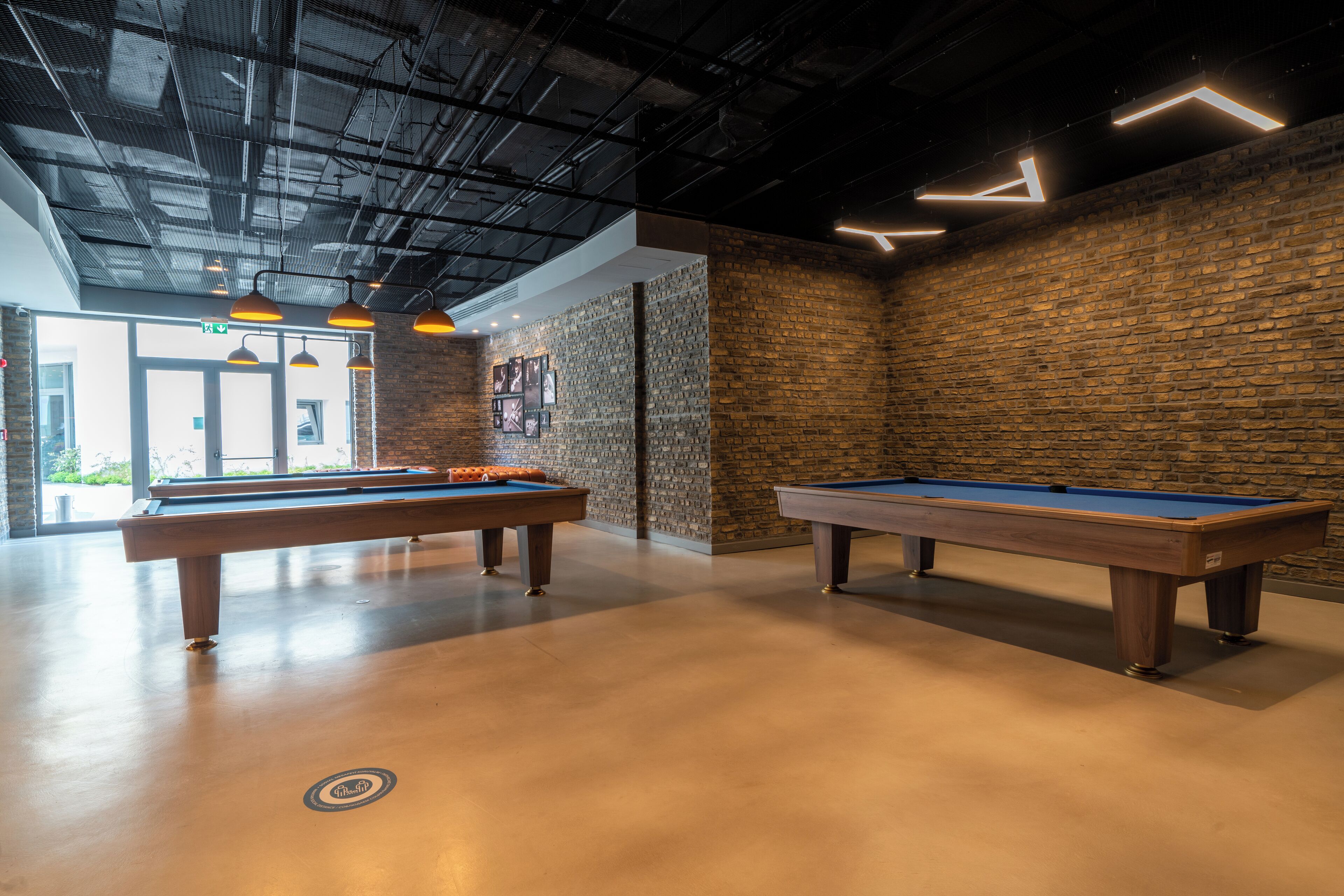Un espace dédié au billard, comprenant deux tables de billard, un mur en briques et des lampes suspendues.
