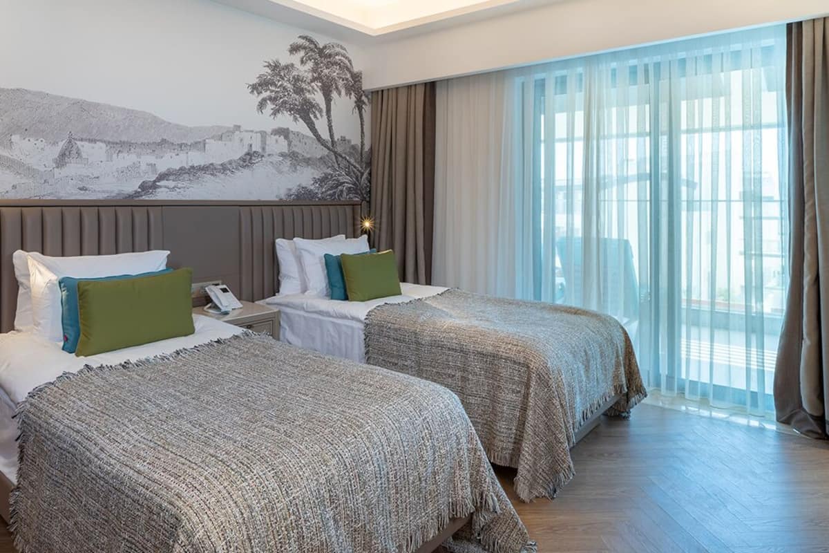 Une chambre d’hôtel avec deux lits, une grande fenêtre avec des rideaux et une fresque murale.