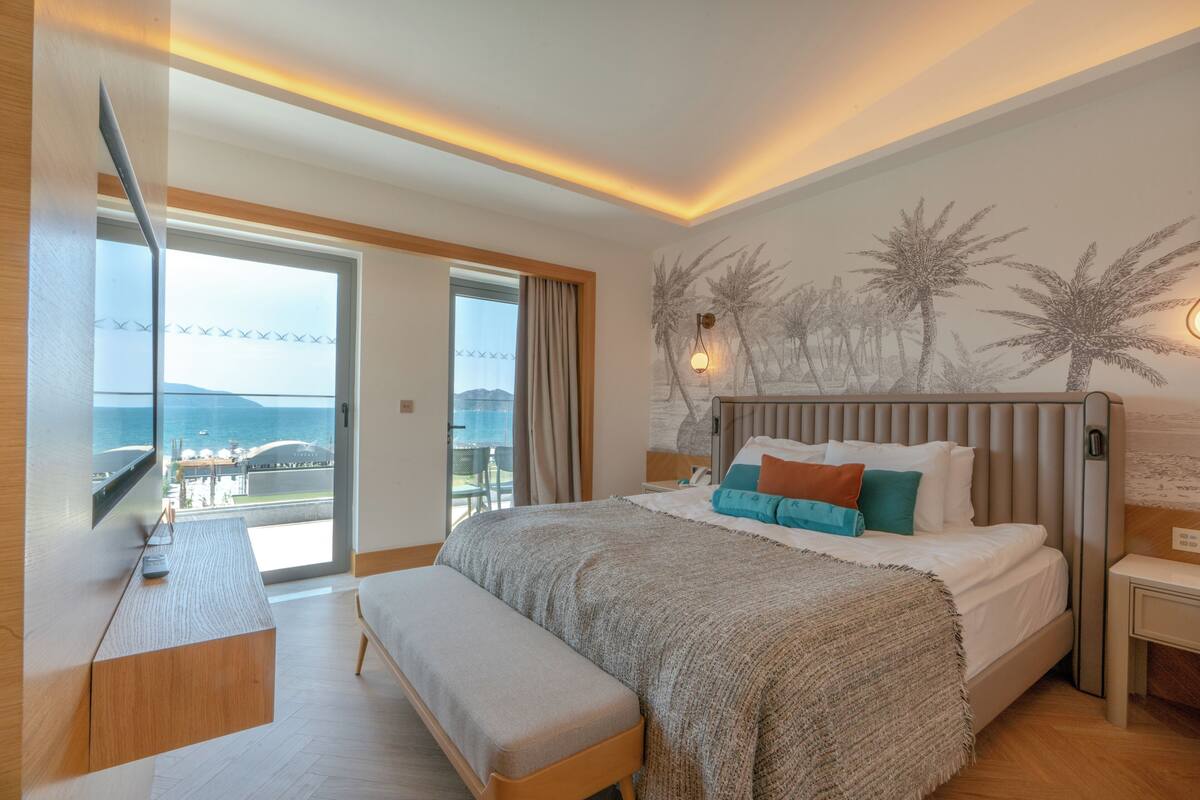 Une chambre d’hôtel moderne dotée d’un grand lit, d’une banquette, d’un bureau et offrant une vue sur la mer.