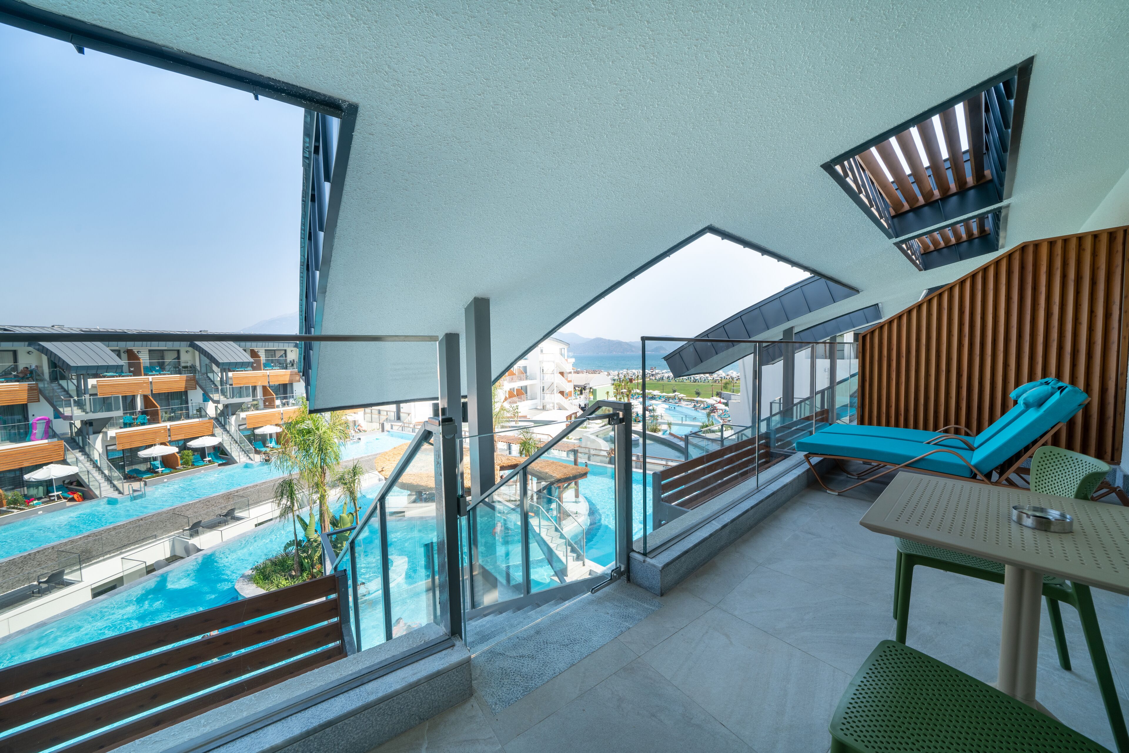 A balcony with a view of a swimming pool and a lounge area with a table and chairs.