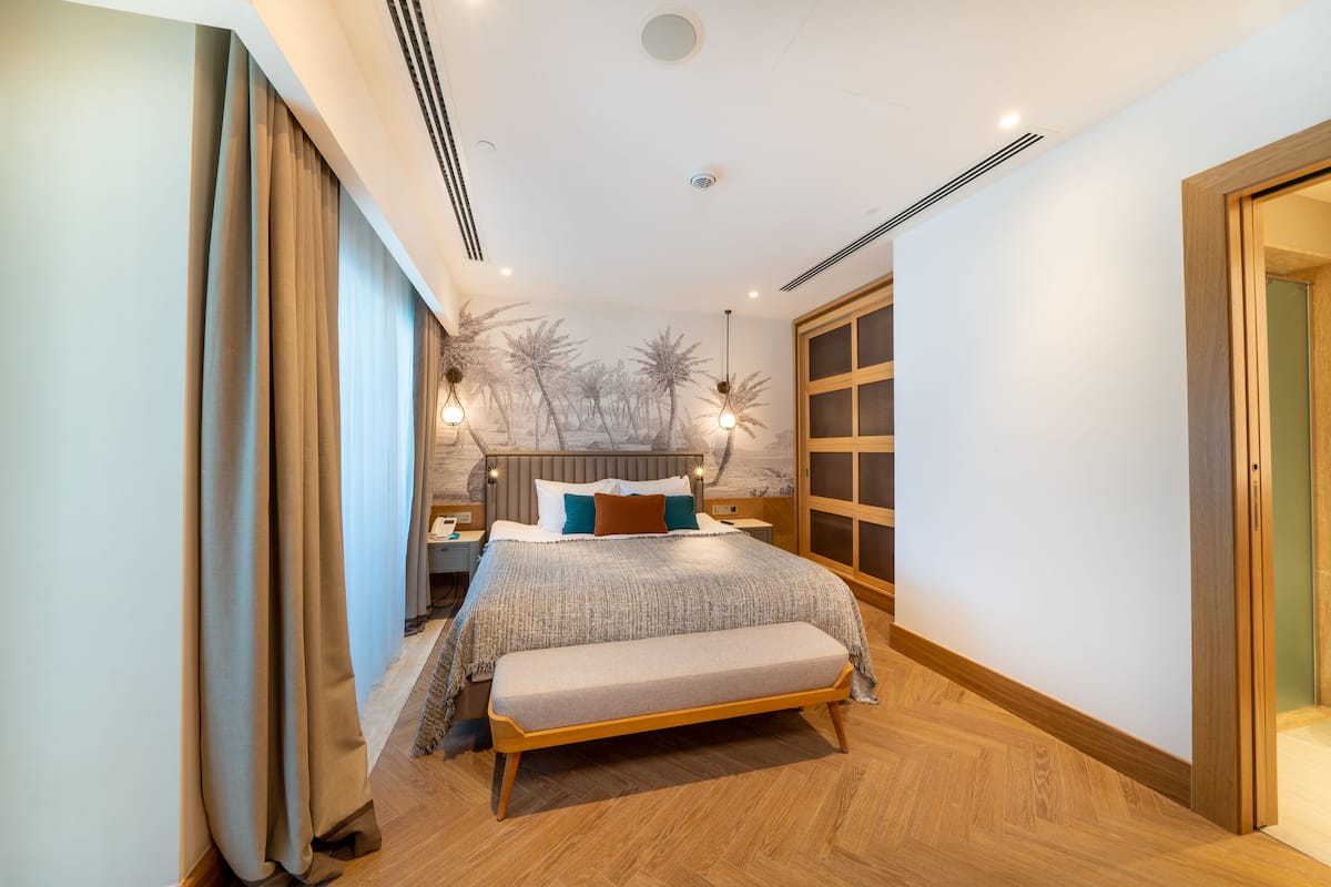 Une chambre à coucher moderne avec un grand lit, un banc, une table de chevet et une lampe fixée au mur.