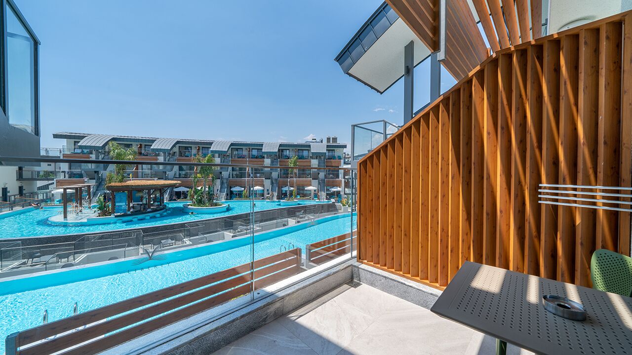 A balcony with a view of a swimming pool and a covered area, overlooking a modern building complex.