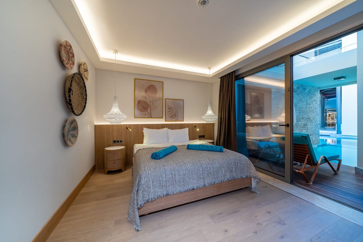 Une chambre moderne avec un grand lit, des tables de chevet et une vue sur une piscine, visible à travers une porte vitrée.