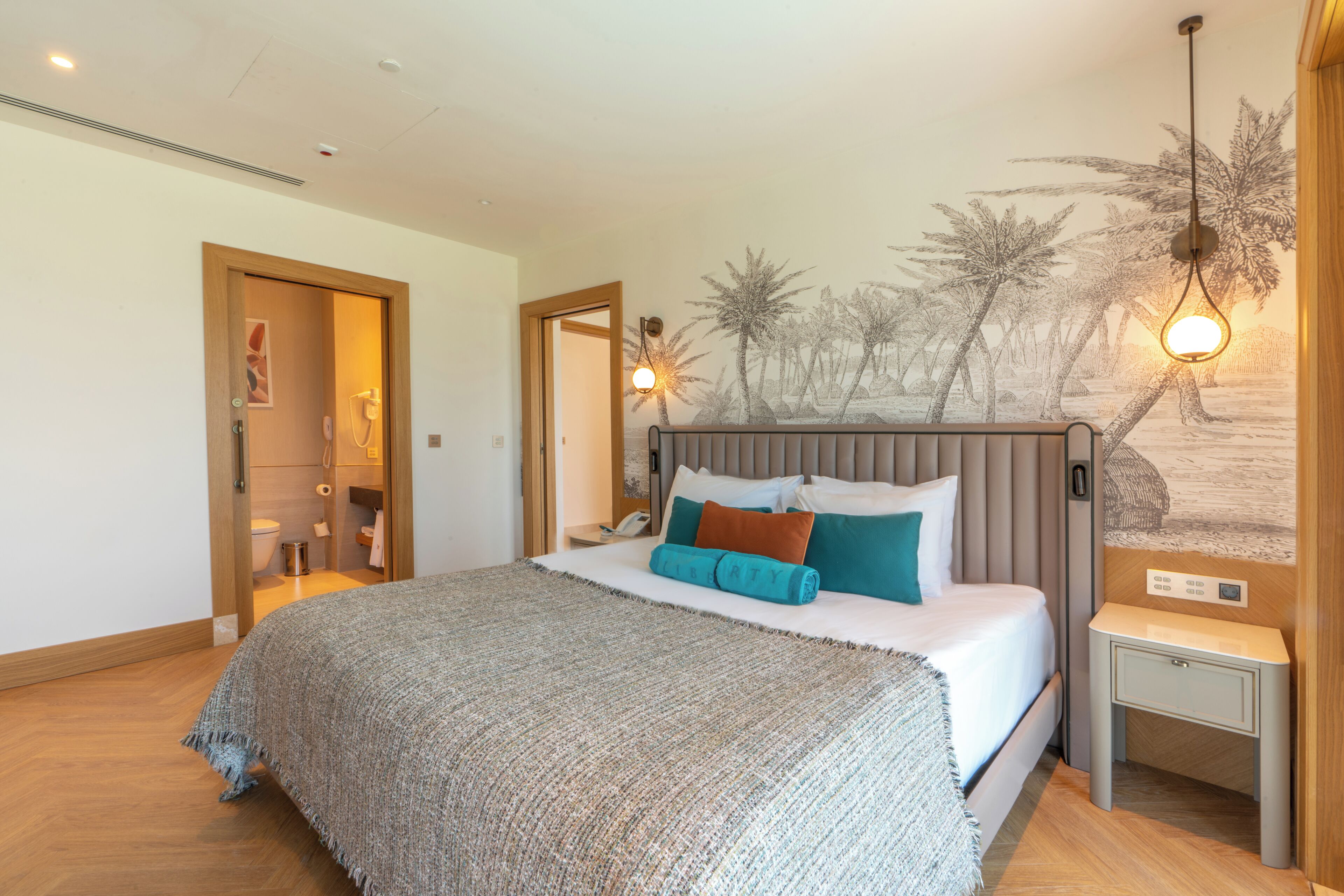 A bedroom with a bed, a nightstand, a wall-mounted lamp, and a mural of palm trees.