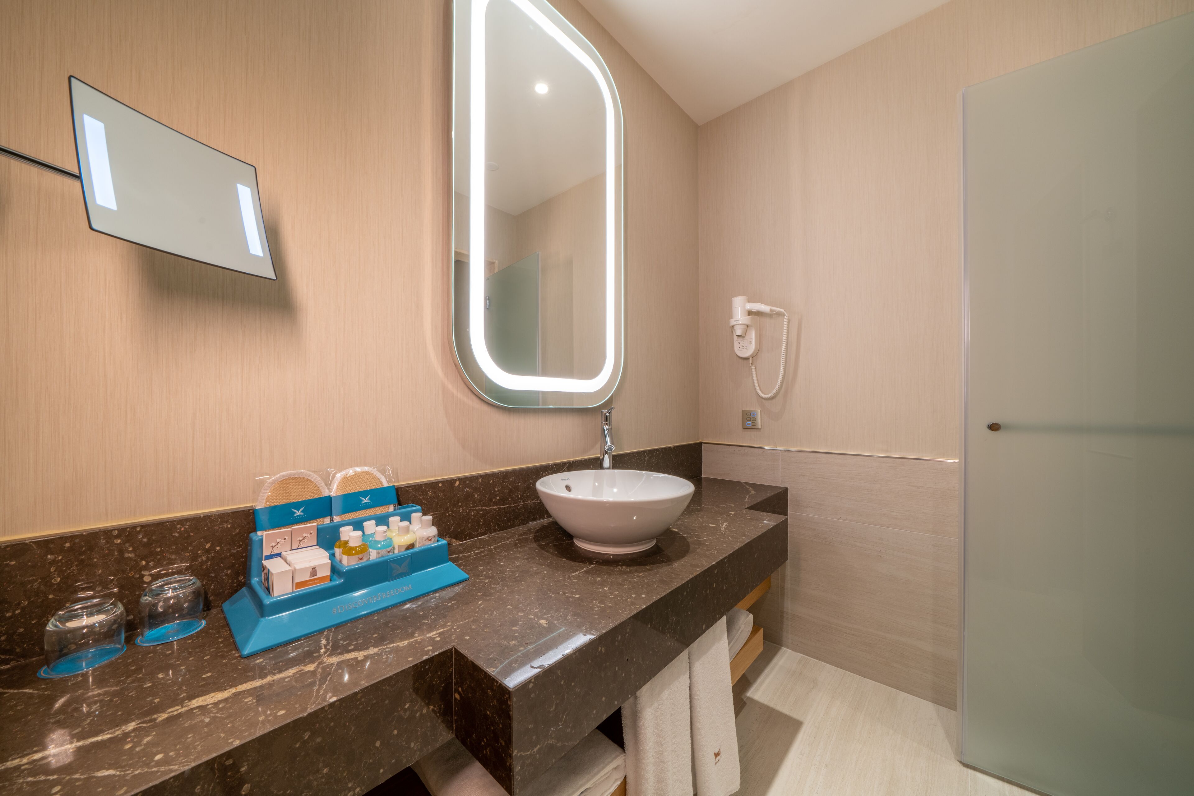 A bathroom with a marble countertop, a white sink, a mirror with light, and a hairdryer.