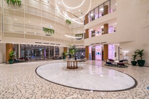 A spacious lobby with a central marble floor, multiple seating areas, and hanging plants.