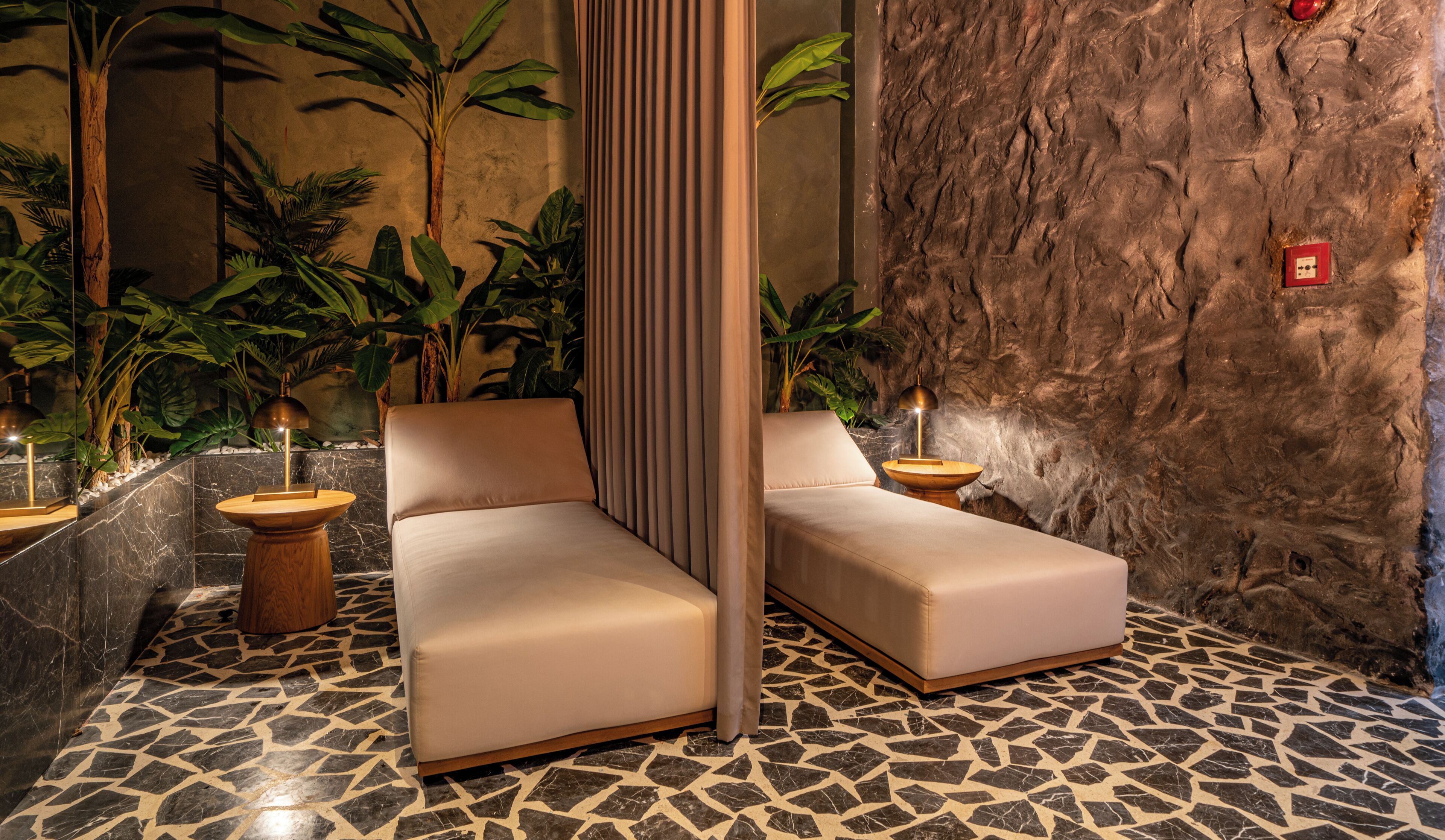 Un área de spa con dos zonas de asientos acolchados, suelo de mármol y pared con textura que imita a la roca.
