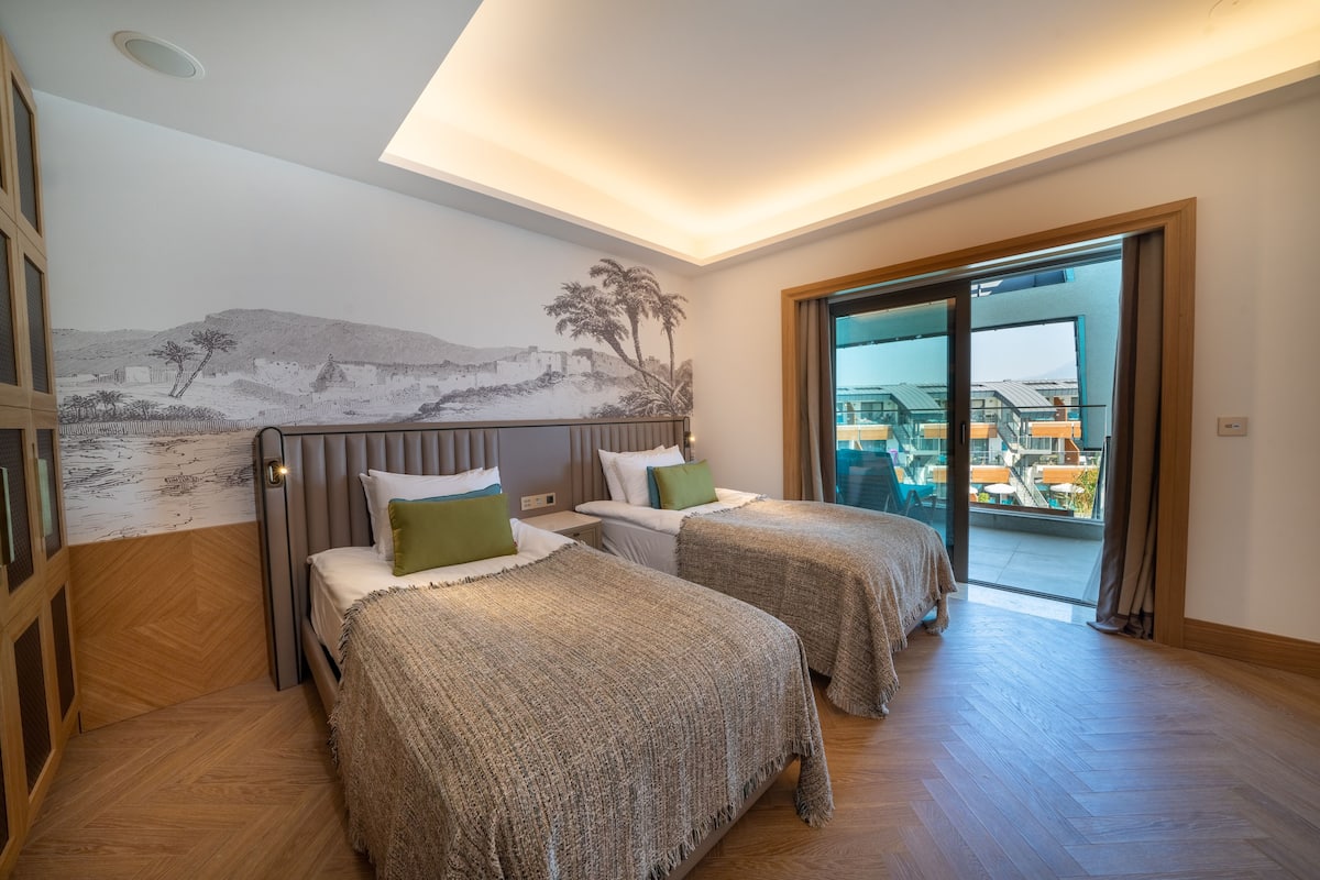 Une chambre d’hôtel avec deux lits, une fresque murale et un balcon avec vue.