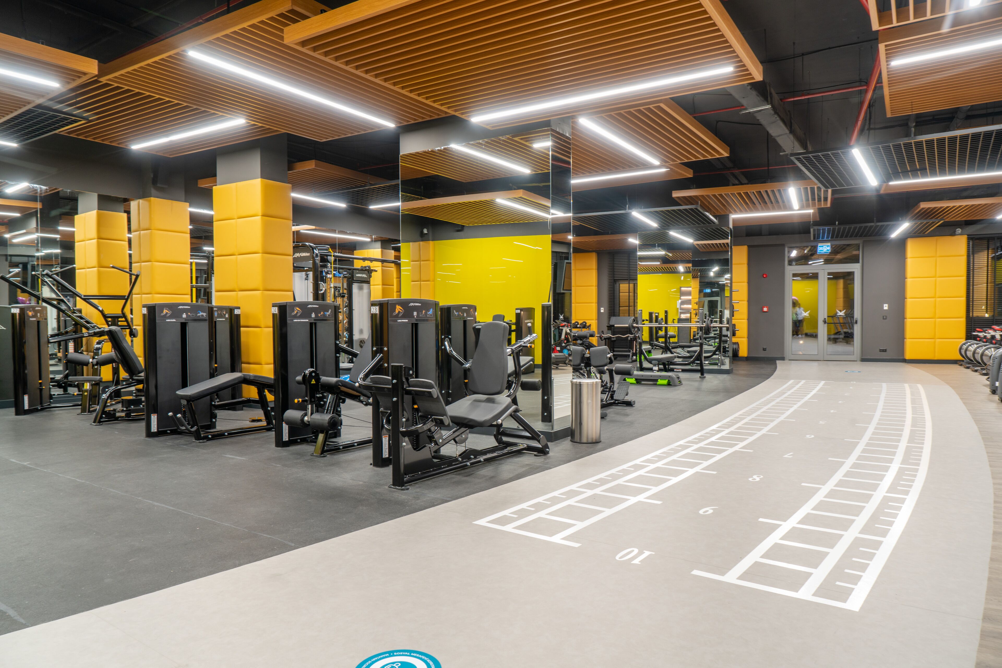 Un gimnasio con equipo de ejercicio, un espejo grande y una decoración en tonos amarillo y gris.