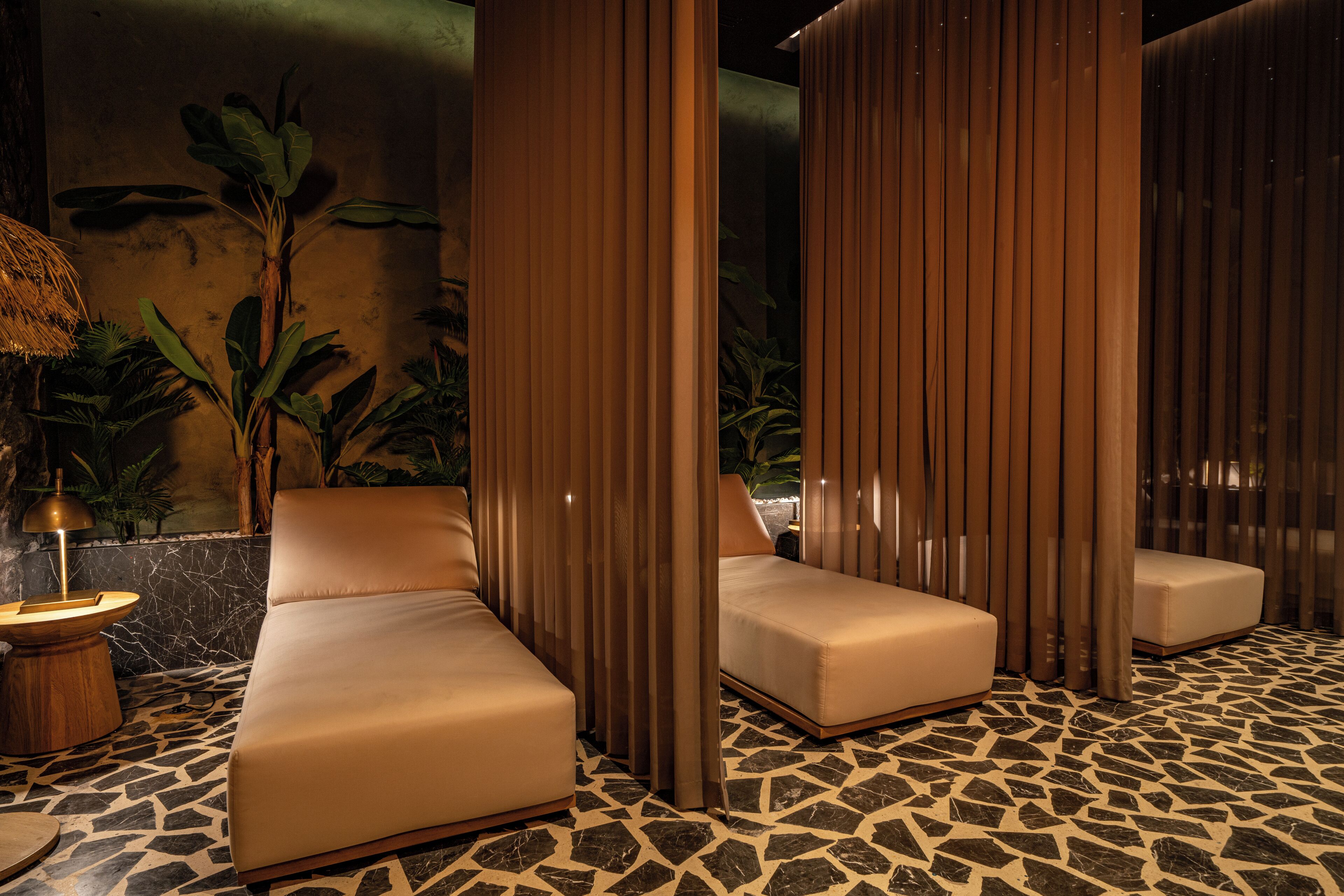 A spa area with three cushioned seating areas, a stone-tiled floor, and a tropical plant backdrop.