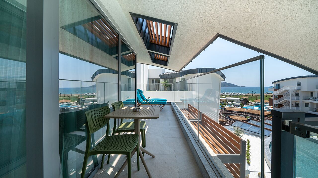 Un balcón con mesa y sillas, una sillón azul y vista al mar y edificios.