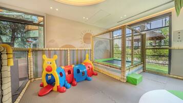 A play area with a colorful train set, padded flooring, and a view of the outdoors through a large window.