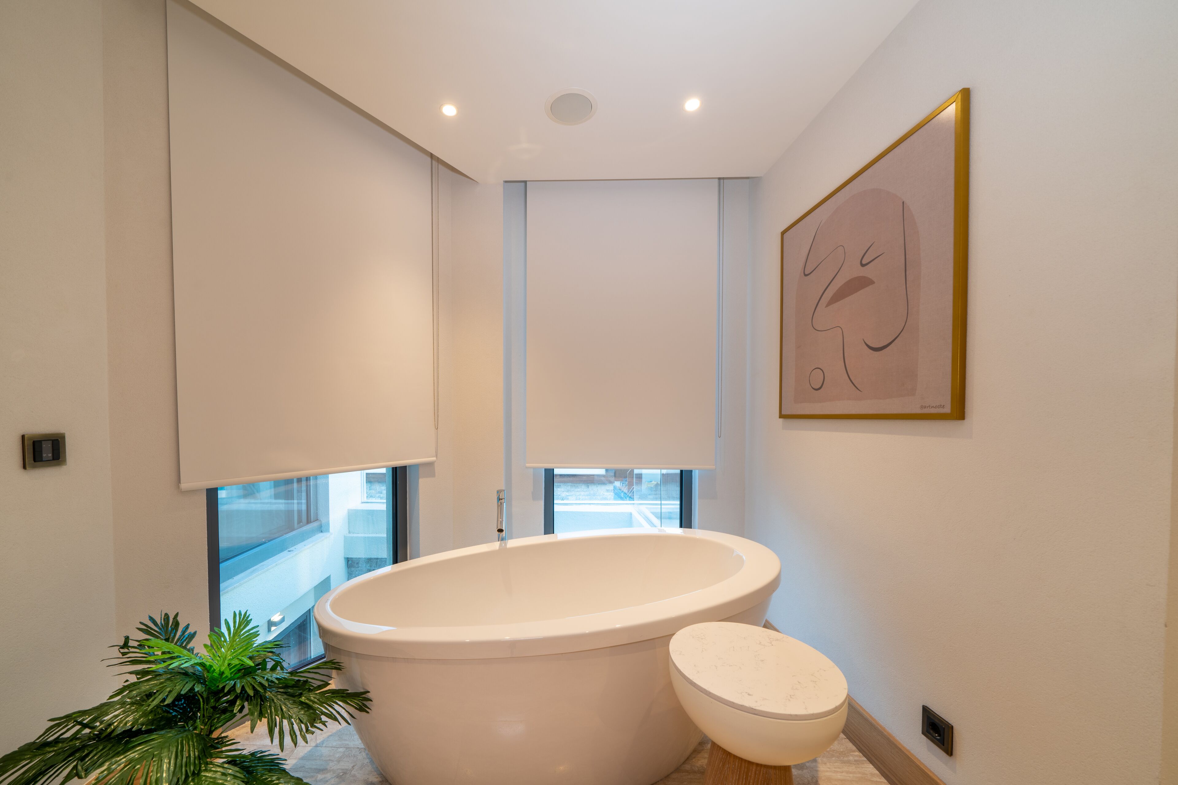 A modern bathroom with a freestanding bathtub, a toilet, and a potted plant.