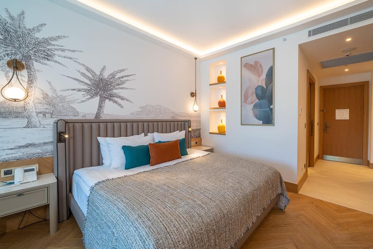 Une chambre moderne avec un grand lit, des tables de chevet, un bureau et une étagère murale agrémentée d’objets décoratifs.