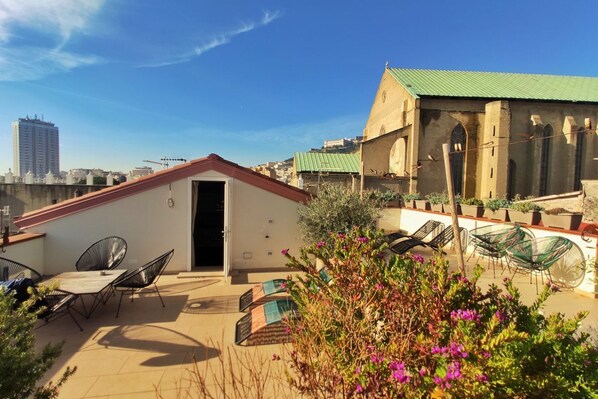 A rooftop terrace with outdoor seating, a small building with a door, and a church in the background.