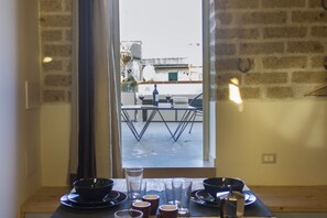 A dining area with a table set for two, a window with curtains, and a view of the street outside.