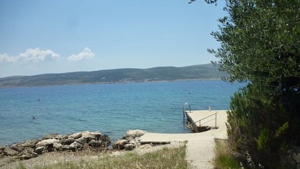 Un sentier côtier menant à une plage rocheuse, bordée d’une rambarde métallique et surmontée d’un quai en béton.